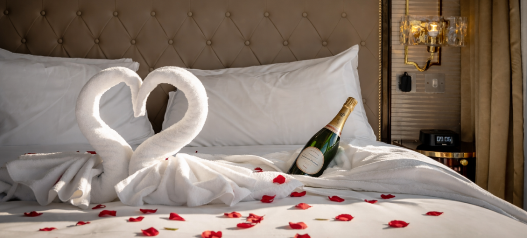 Champagne and rose petals on a bed in a hotel suite