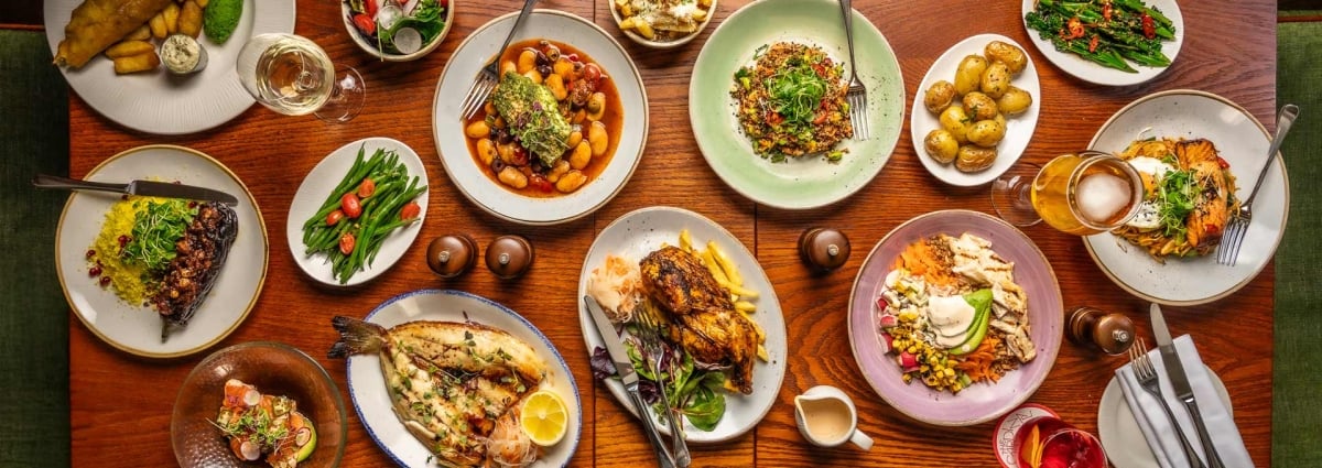 Lots of dishes on a wooden table such as salad, fish and chips and fries