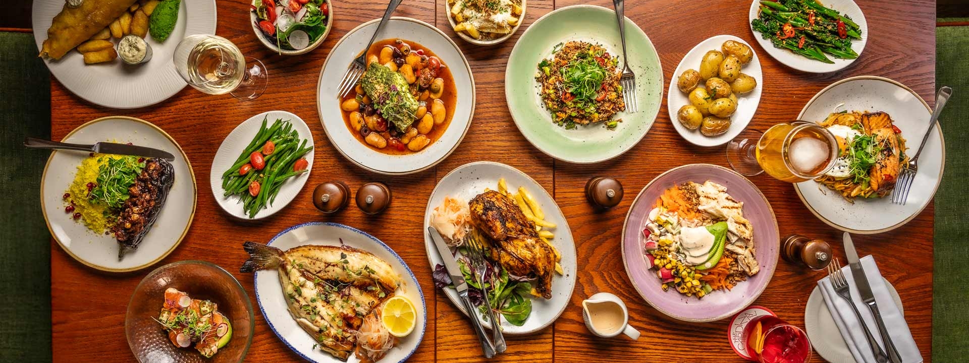 Lots of dishes on a wooden table such as salad, fish and chips and fries
