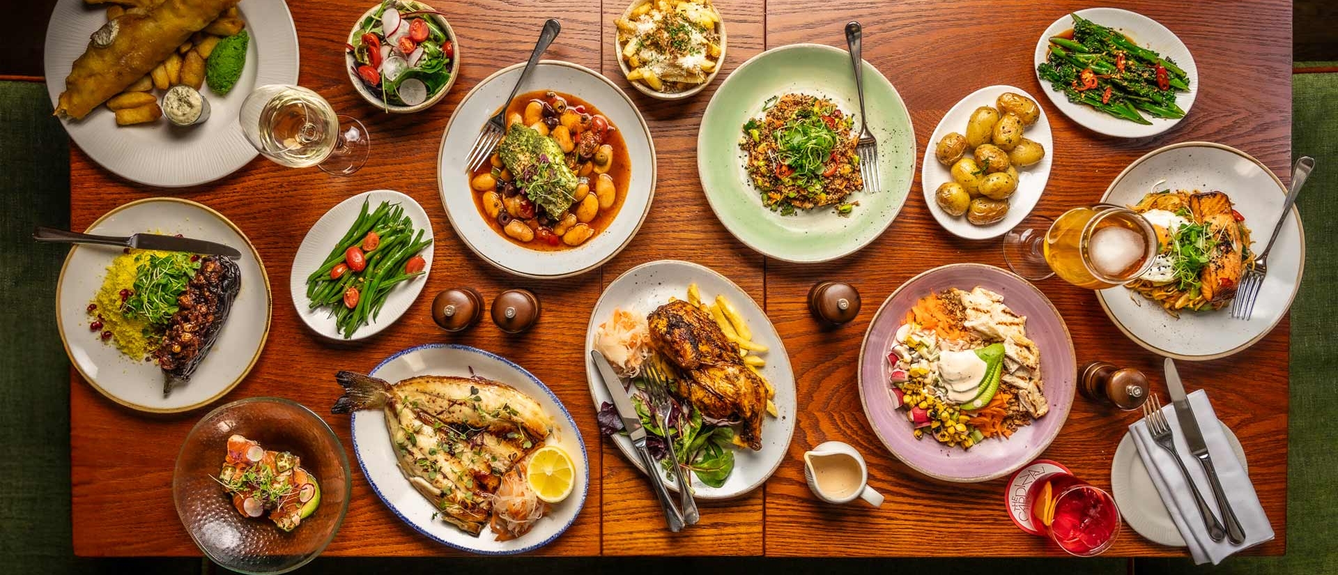 Lots of dishes on a wooden table such as salad, fish and chips and fries