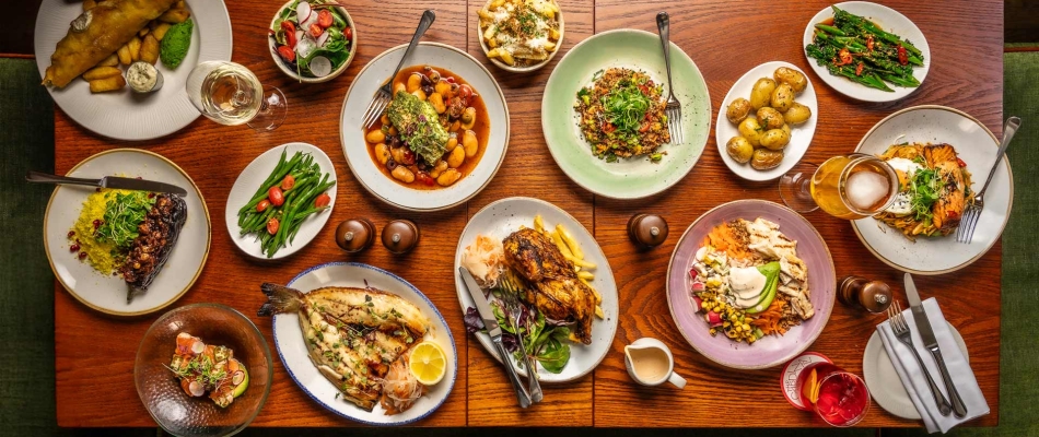 Lots of dishes on a wooden table such as salad, fish and chips and fries