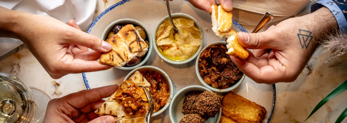 Hands picking at a mezze platter filled with hummus, halloumi and pita bread