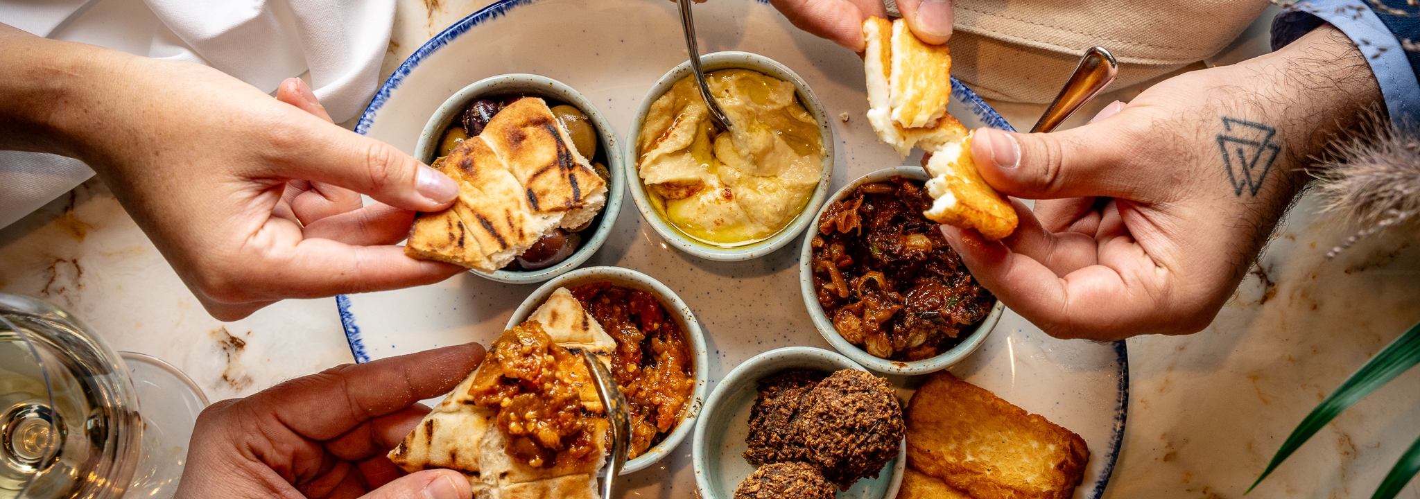 Hands picking at a mezze platter filled with hummus, halloumi and pita bread