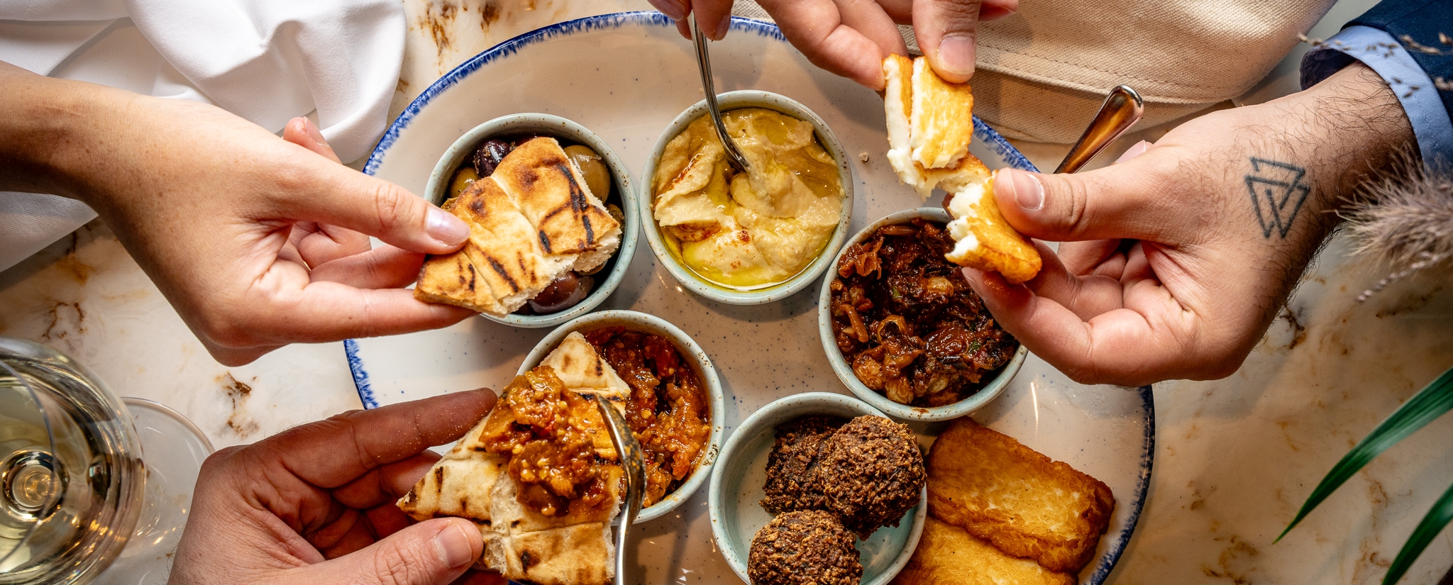 Hands picking at a mezze platter filled with hummus, halloumi and pita bread