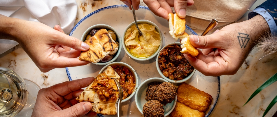 Hands picking at a mezze platter filled with hummus, halloumi and pita bread
